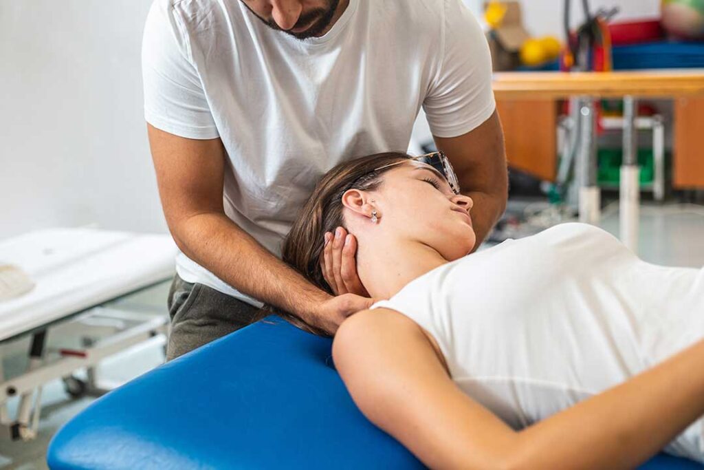 A person sitting at a desk with shoulders hunched, holding the back of their neck in discomfort.